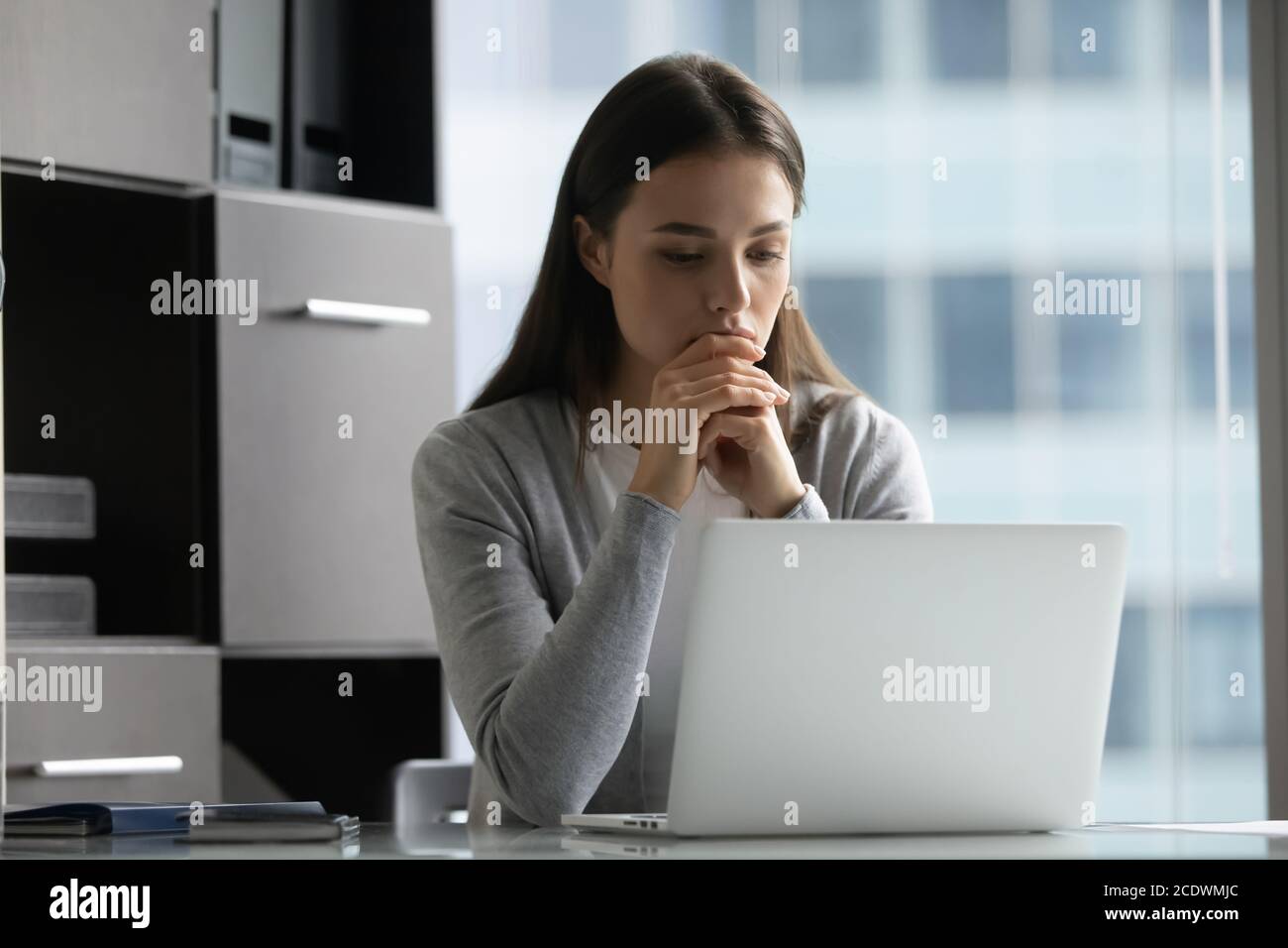 Thoughtful focused young businesswoman looking at laptop screen in office Stock Photo