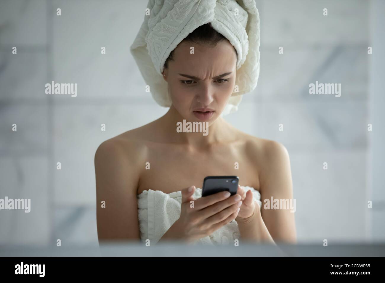 Unhappy young woman reading bad news in message in bathroom Stock Photo