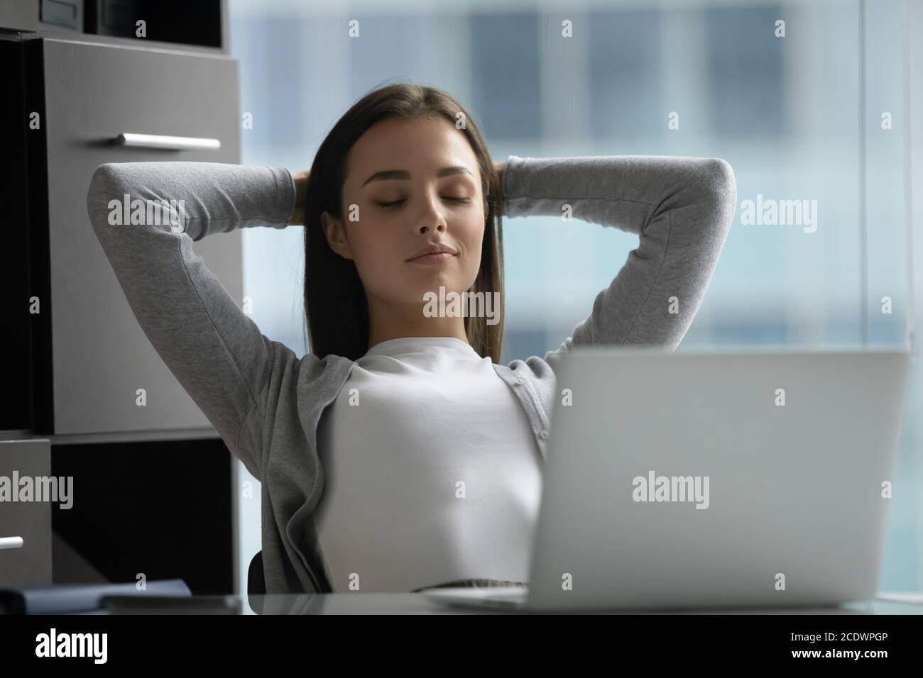 Peaceful satisfied young businesswoman stretching hands, relaxing in office Stock Photo