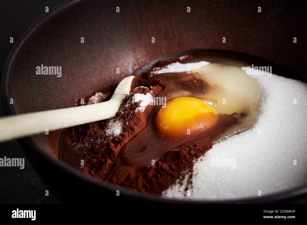 Mixing Bowl with Wooden Spoon, Egg, Cocoa and Sugar Stock Photo