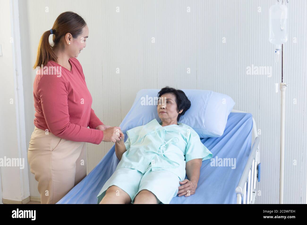 An Asian woman takes care of her sick mother in bed in a hospital. Stock Photo