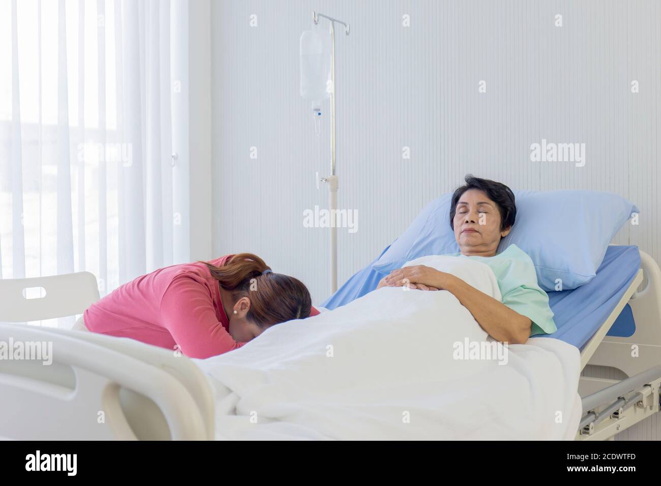An elderly Asian woman is sick and sleeps in the bed next to Her daughter slept in the care of her hospital bed. Stock Photo