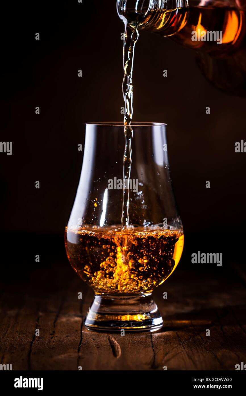 Scotch Whiskey without ice pouring out of the bottle, rustic wood background, copy space Stock