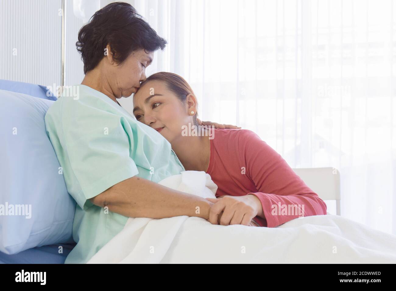 An Asian daughter takes care of her sick mother on a bed in a hospital ...
