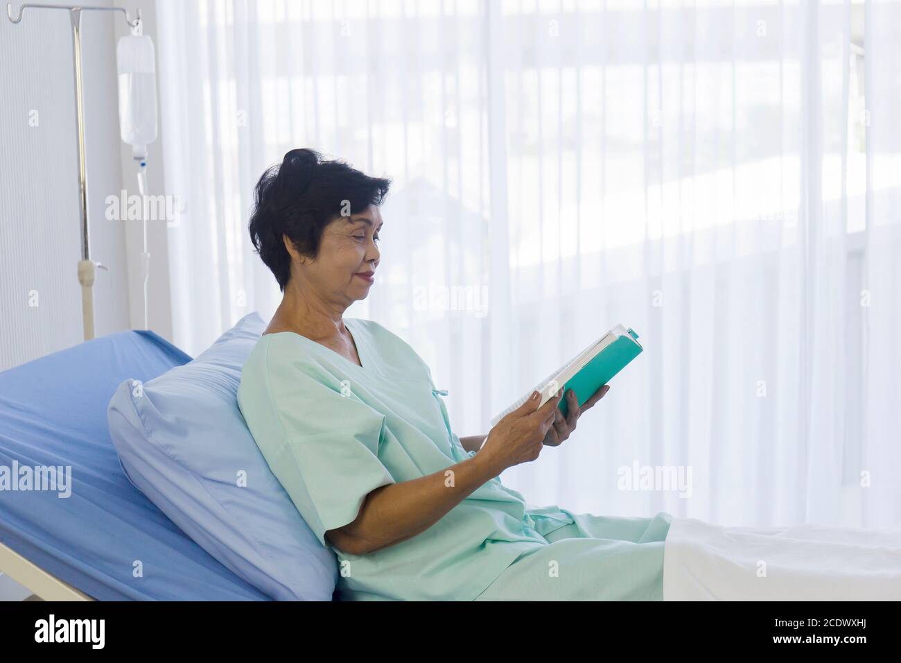 The elderly Asian women sat on the bed to read in the hospital. Stock Photo
