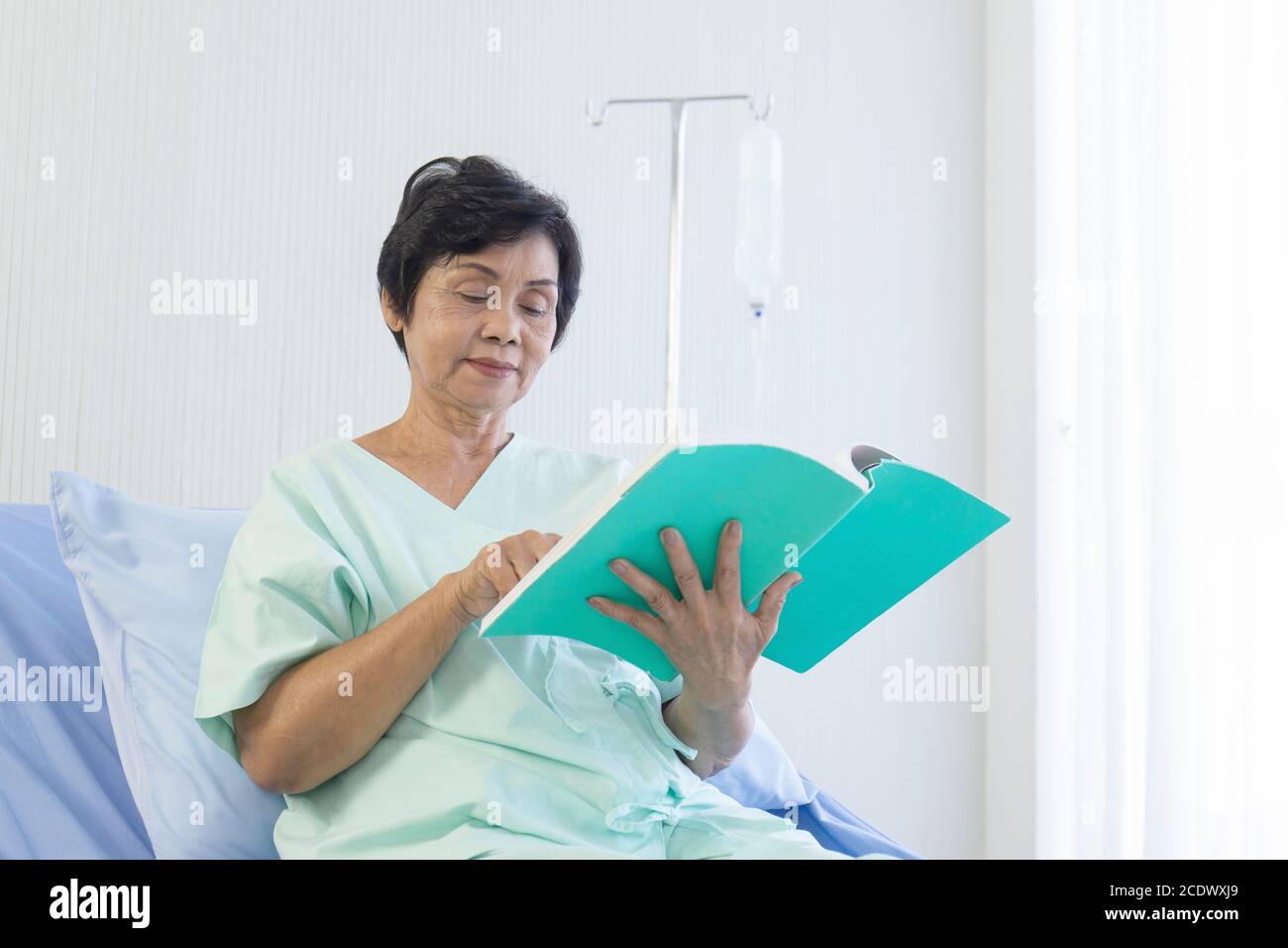 The elderly Asian women sat on the bed to read in the hospital. Stock Photo