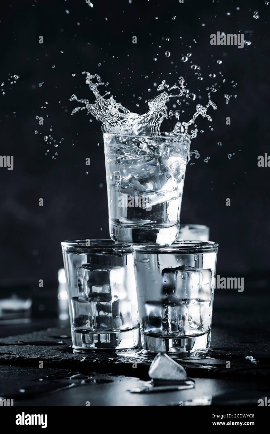 Vodka splash with spray from shot glasses on black stone background, iced strong drink in misted glass Stock Photo