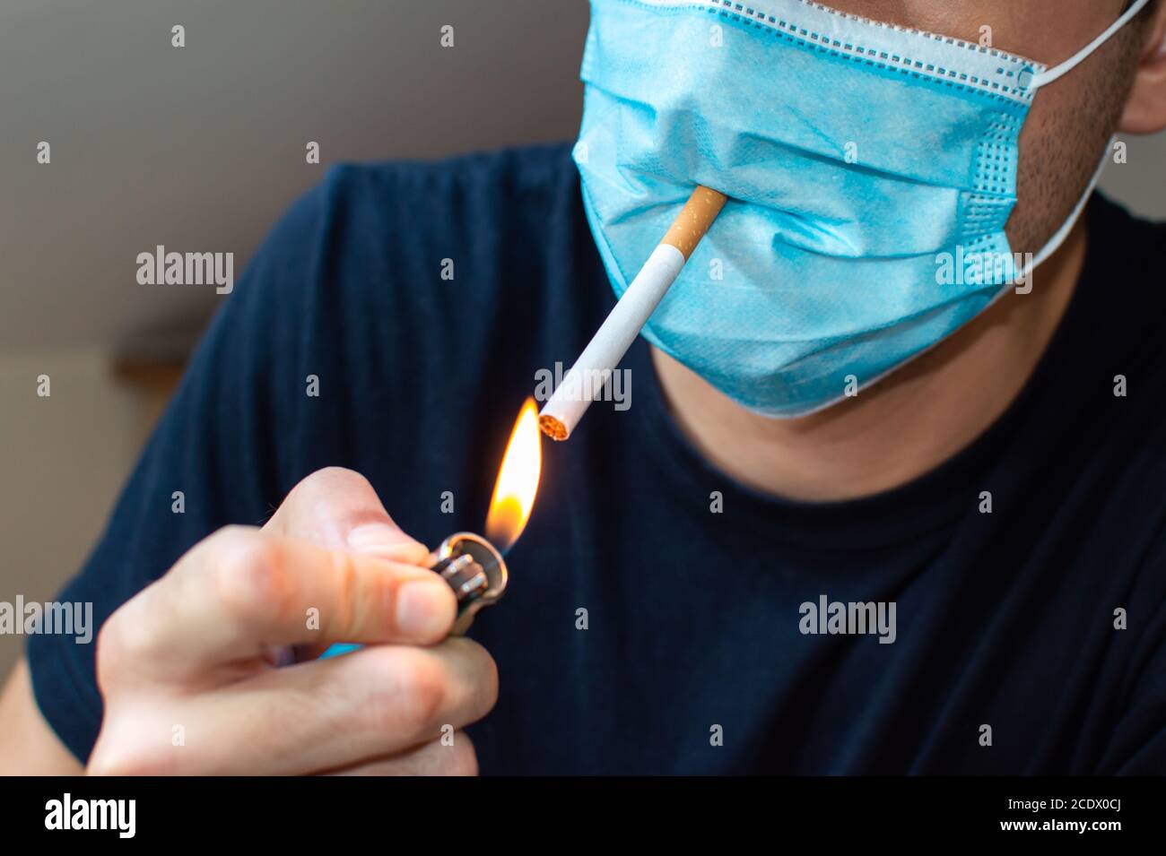 smoking cigarettes with covid Young man with mask lighting a cigarette. Coronavirus funny concept Stock  Photo