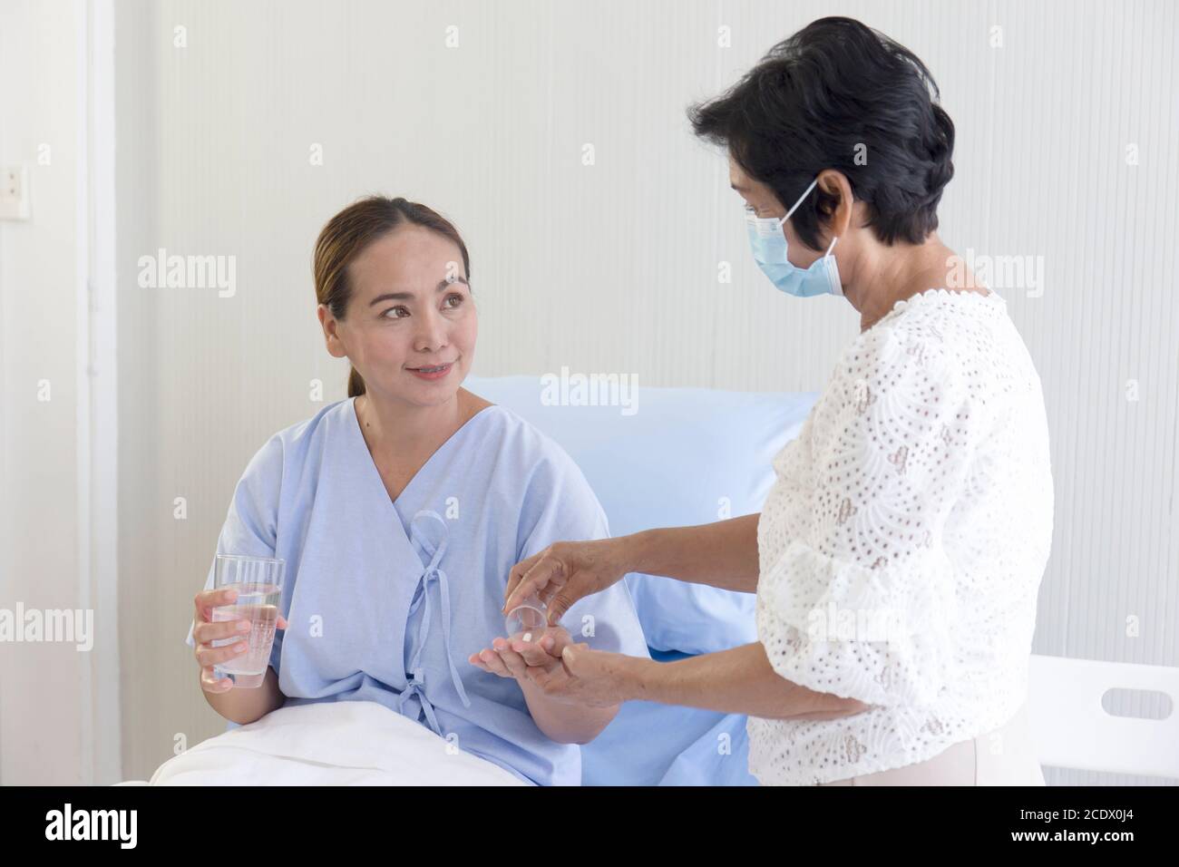 An Asian female patient lying on a bed receiving medication from her mother. Stock Photo