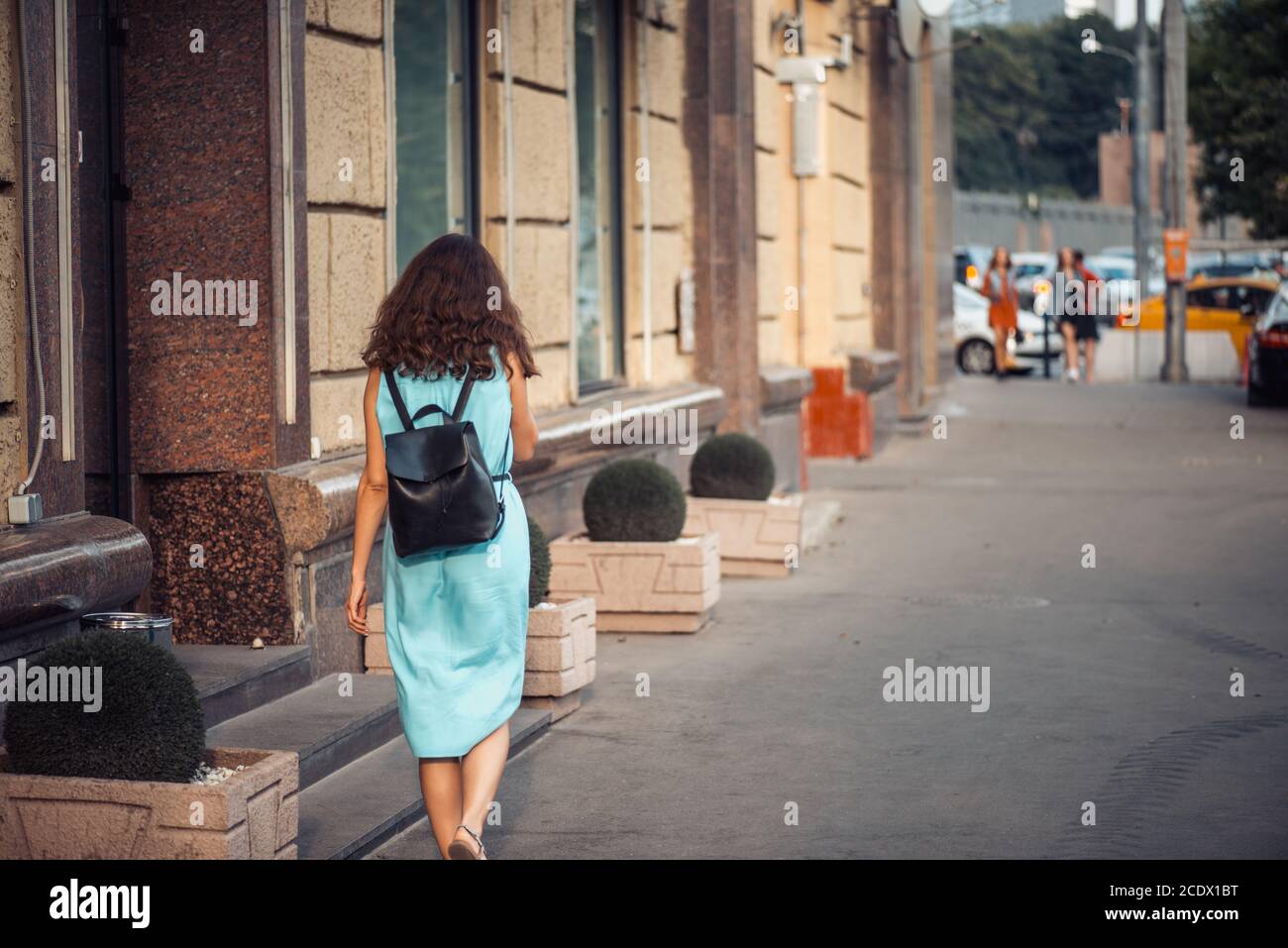 Back view of a hipster girl in a blue dress with black leather backpack ...