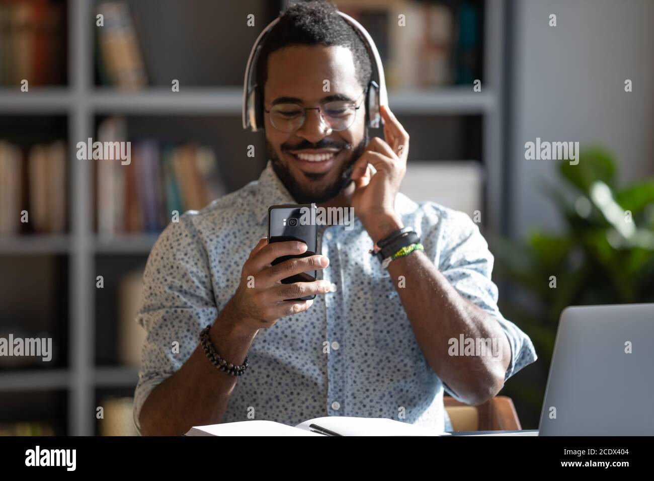 Smiling positive African American man wearing headphones using phone Stock Photo