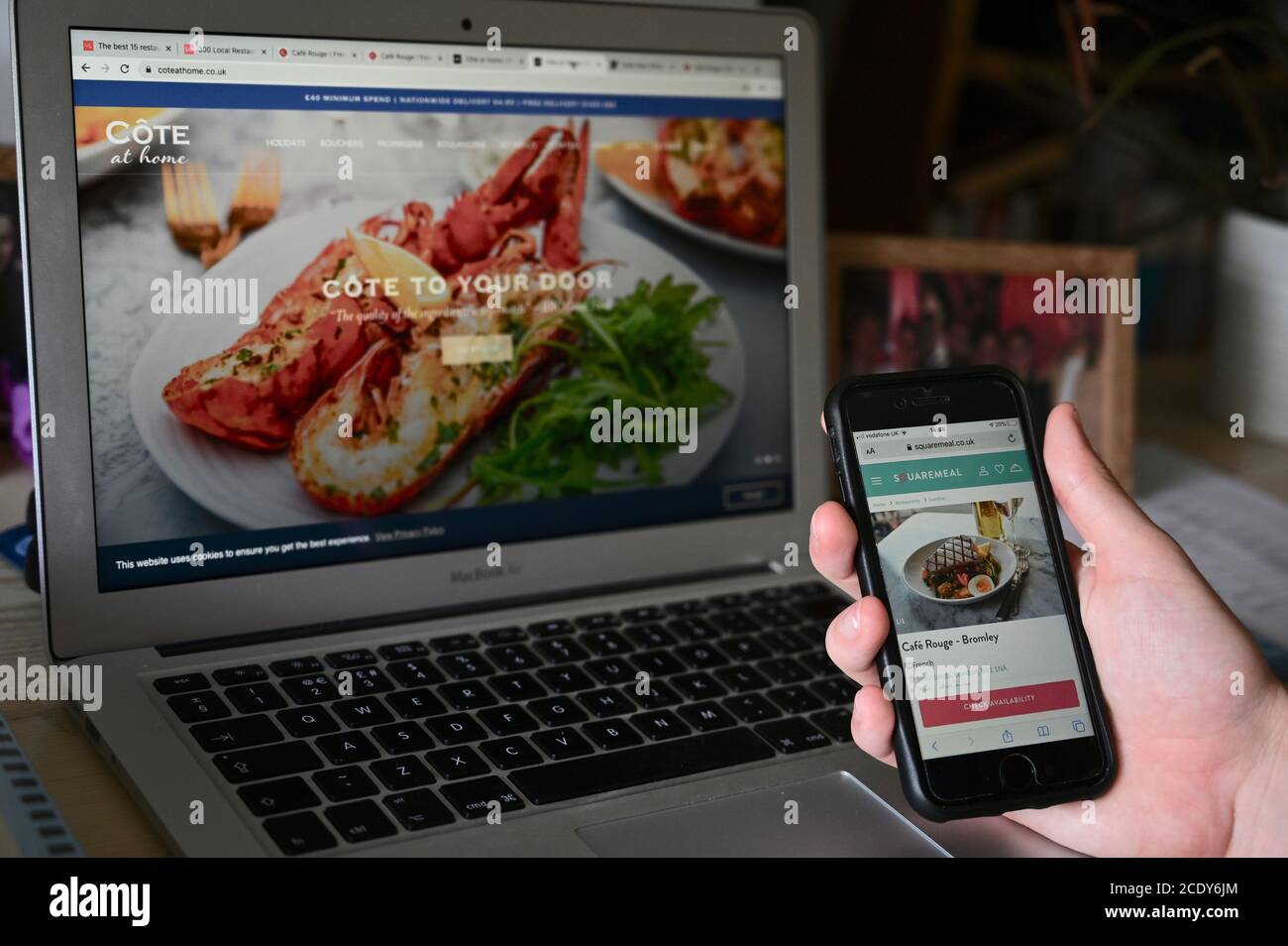 Apple iPhone SE screen with Squaremeal webpage. Macbook air with Cote at home webpage. Stock Photo