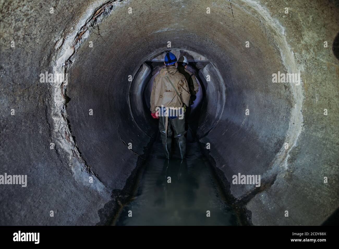 Sewer tunnel worker examines sewer system damage and wastewater leakage Stock Photo
