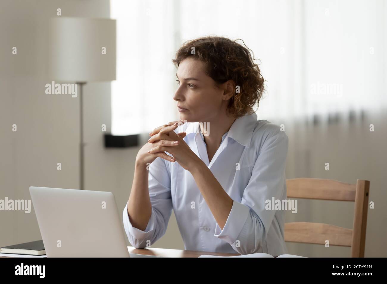 Thoughtful woman doctor sitting at work desk, pondering problem solution Stock Photo