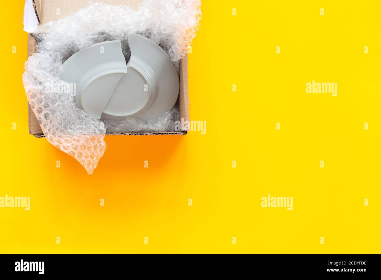 On a yellow background lies an open package, a box with a broken plate Stock Photo