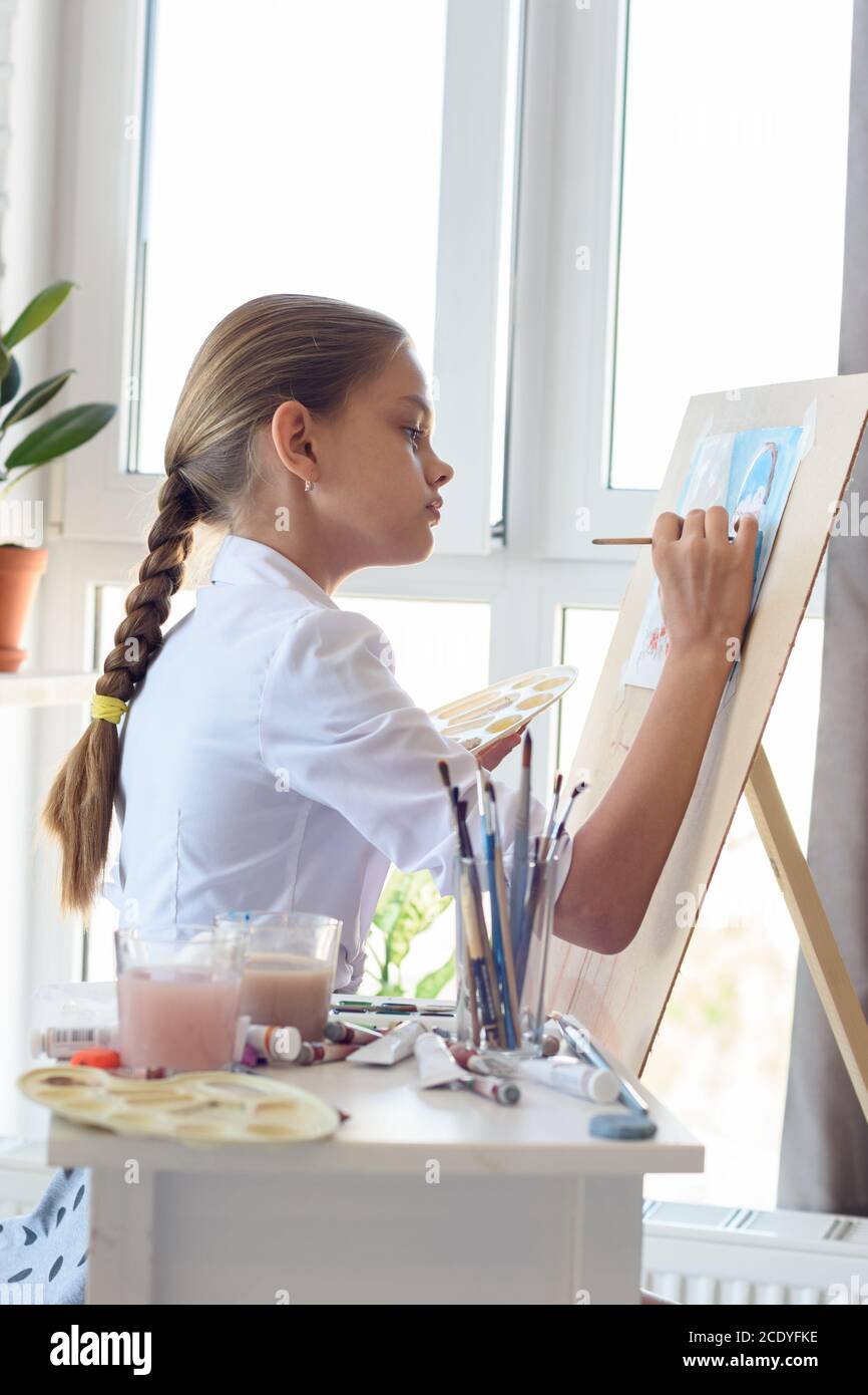 Girl in white shirt draws behind easel with right hand Stock Photo - Alamy