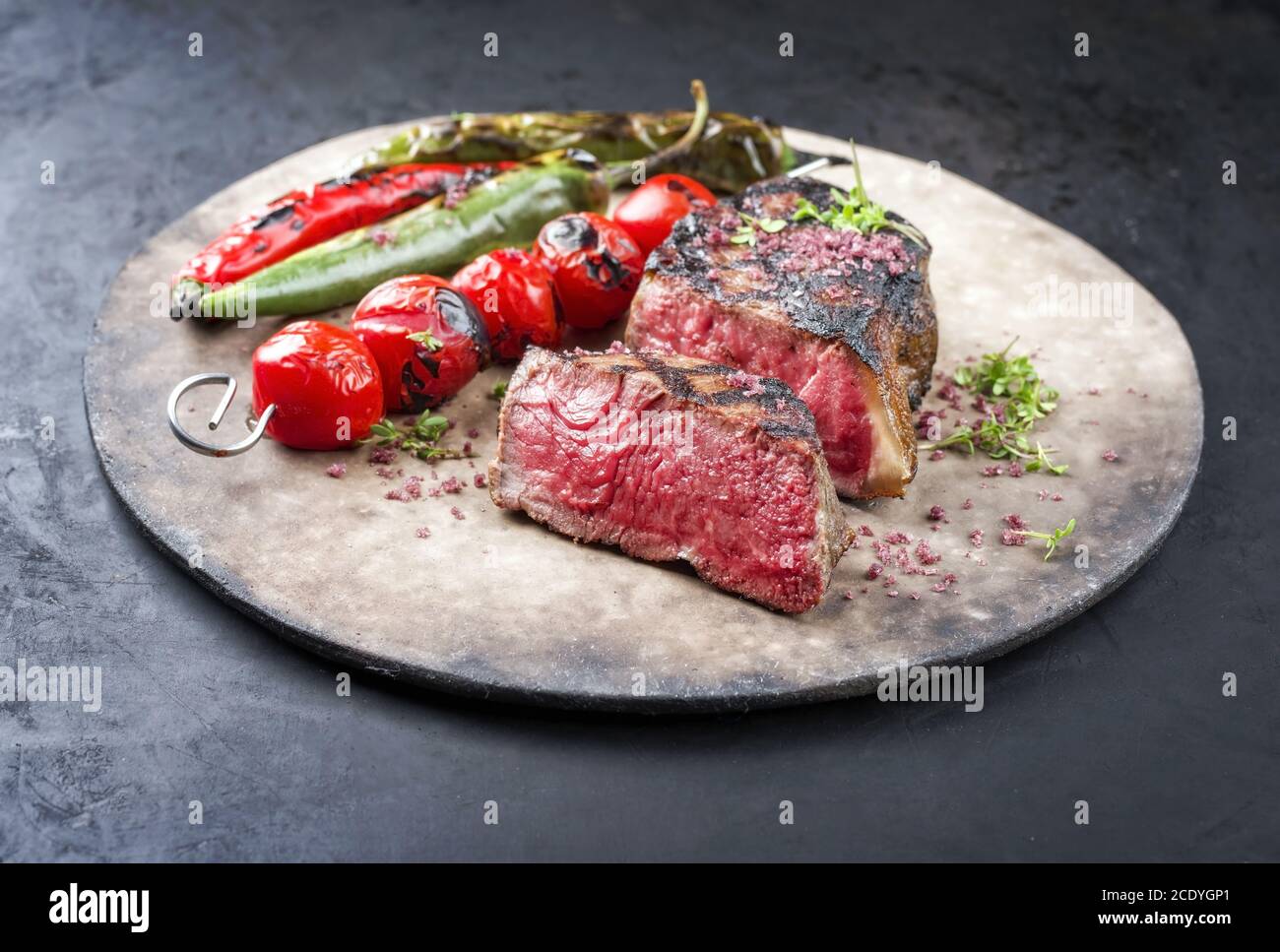 Barbecue dry aged wagyu roast beef steak with tomatoes and chili as closeup on a rustic modern design plate Stock Photo