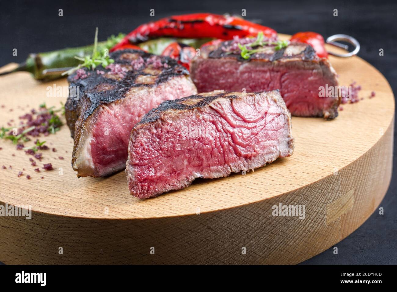 Barbecue dry aged wagyu roast beef steak with tomatoes and chili as closeup on a modern design wooden board Stock Photo