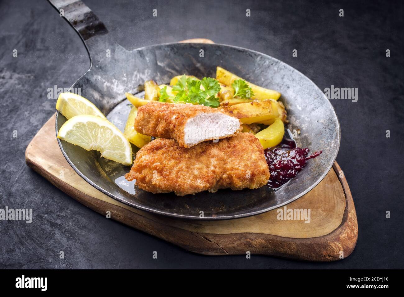 Traditional deep fried veal steak with roast potatoes and cranberry sauce offered as closeup in a rustic old wrought iron skille Stock Photo