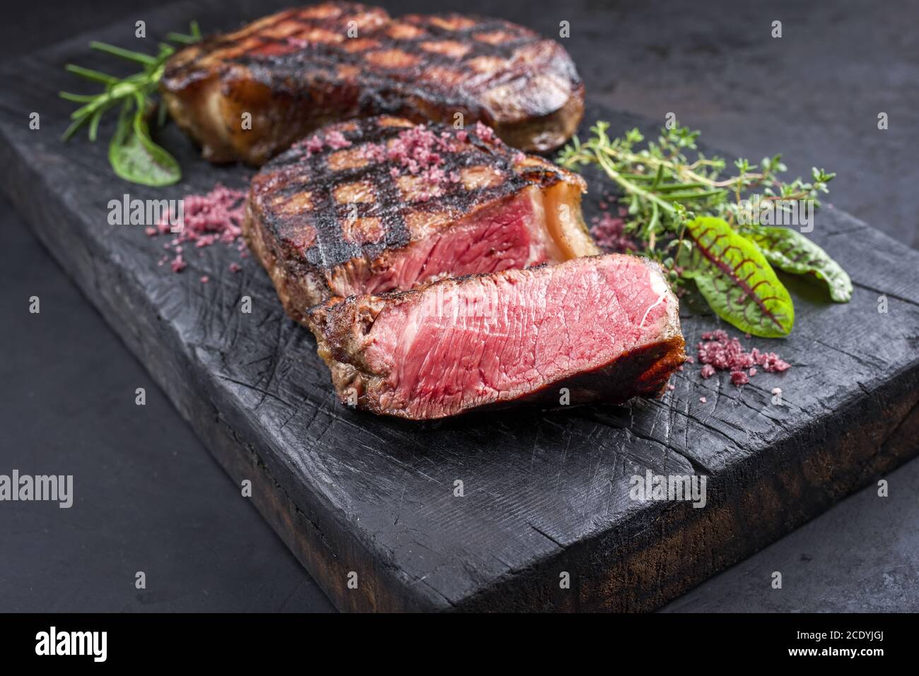 Barbecue dry aged wagyu roast beef steak with lettuce and herbs as closeup on a rustic charred wooden board Stock Photo