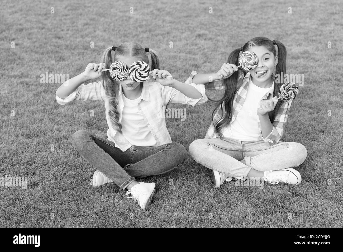 Holiday food. Sweet childhood. Happy children hold candy sit green grass. Candy shop. Lollipop treats. Candy synonym for happiness. Sugar and calories. Joyful cheerful friends eating sweets outdoors. Stock Photo