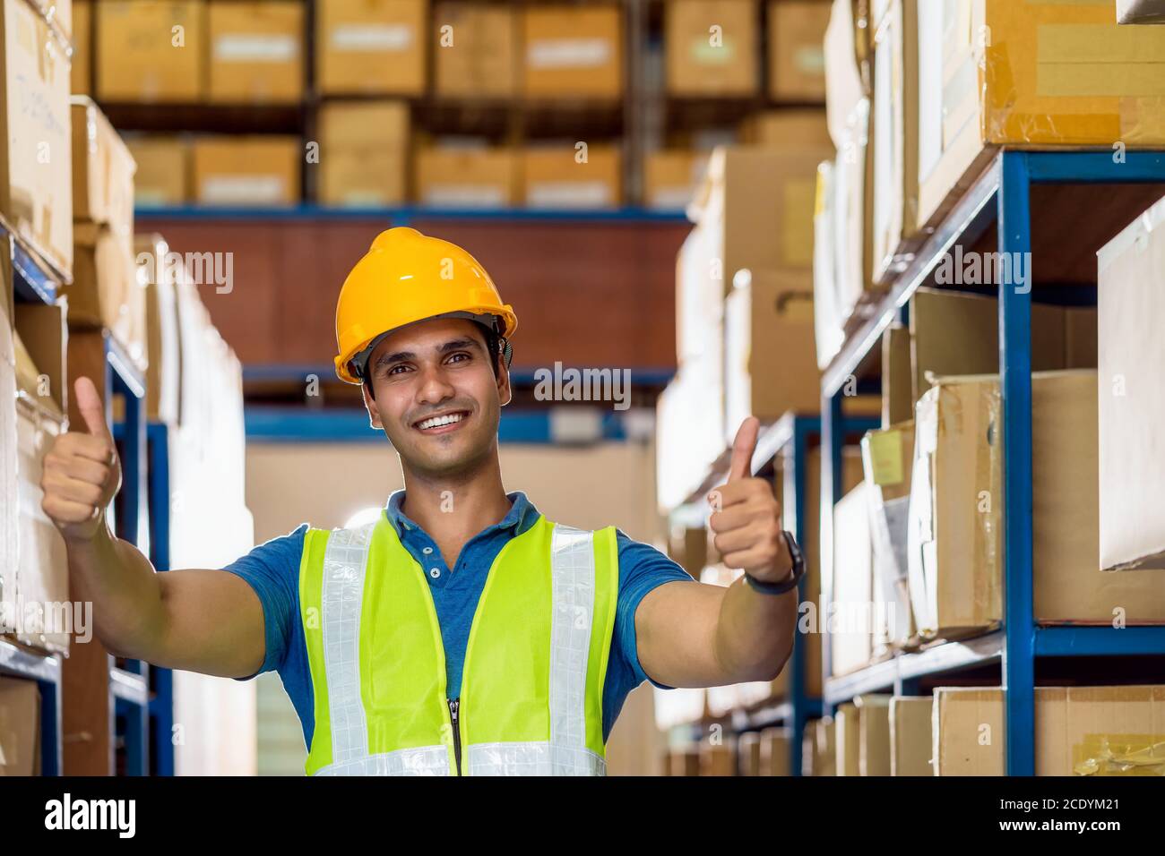 Portrait of Indian warehouse worker man with safety clothes standing with confident and showing thumps up in local workplace with warehouse or factory Stock Photo