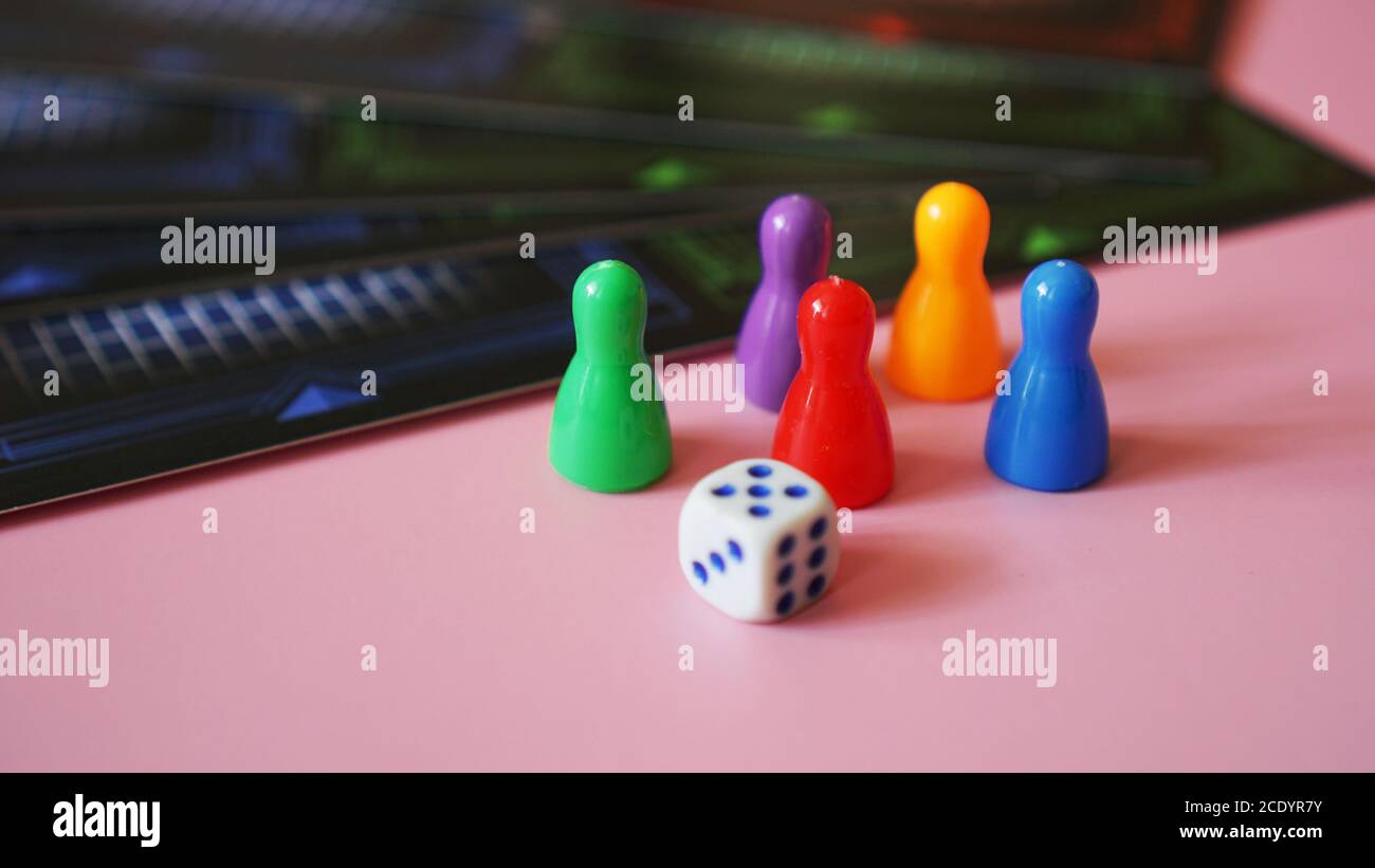 Colored board game figures with dice on pink background Stock Photo