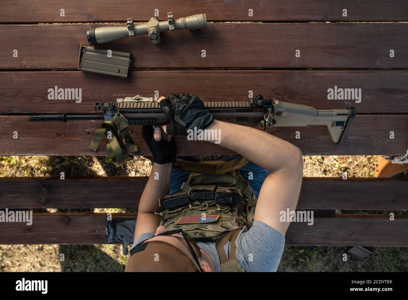 Above view of skilled young American man in gloves sitting at wooden table and assembling rifle while preparing for shooting Stock Photo