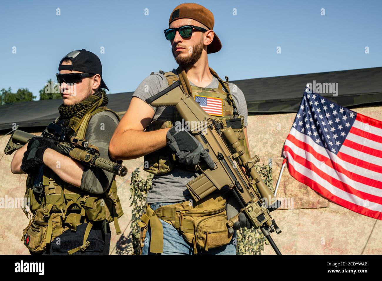 Purposeful young men in sunglasses standing with modern rifles at