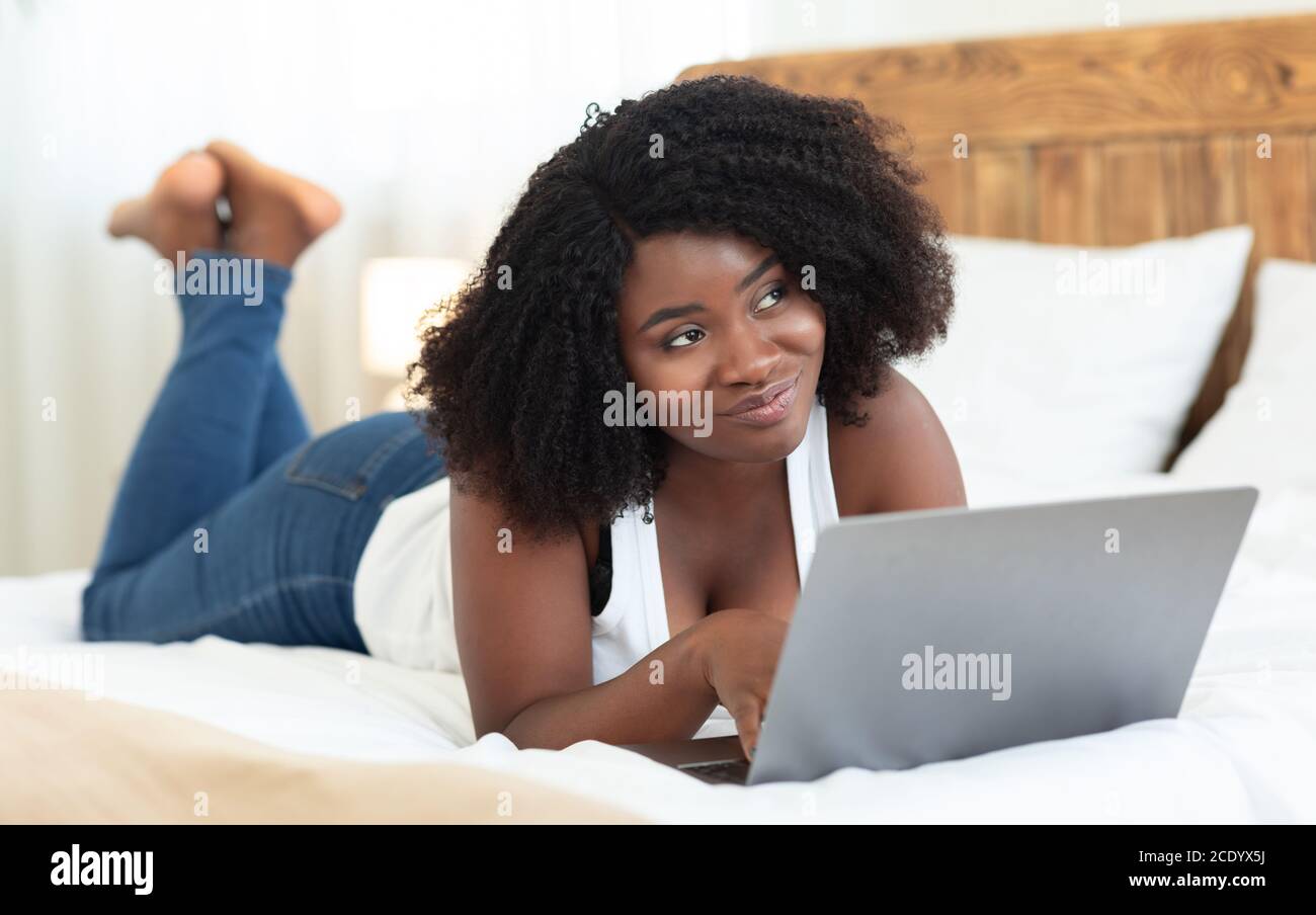 Happy black girl lying on bed, using laptop Stock Photo - Alamy