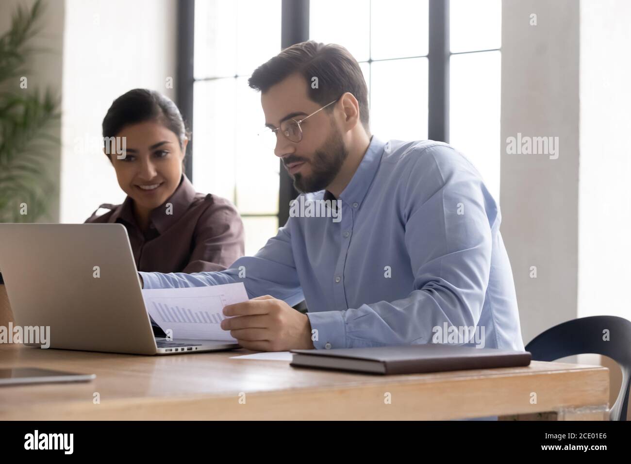 Focused young confident man working on computer with indian colleague. Stock Photo