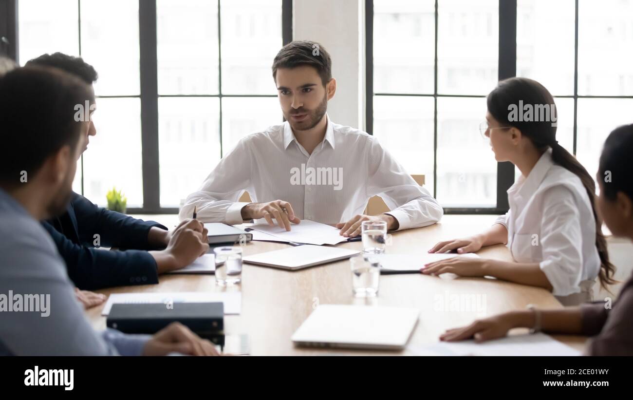 Millennial male mentor instructing mixed race teammates at workplace. Stock Photo