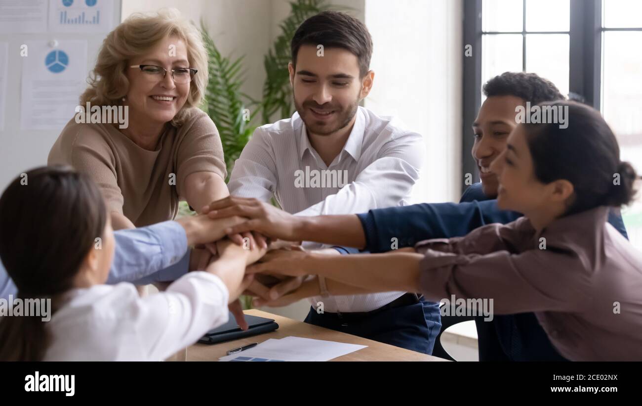 Positive happy young and old mixed race employees joining hands. Stock Photo