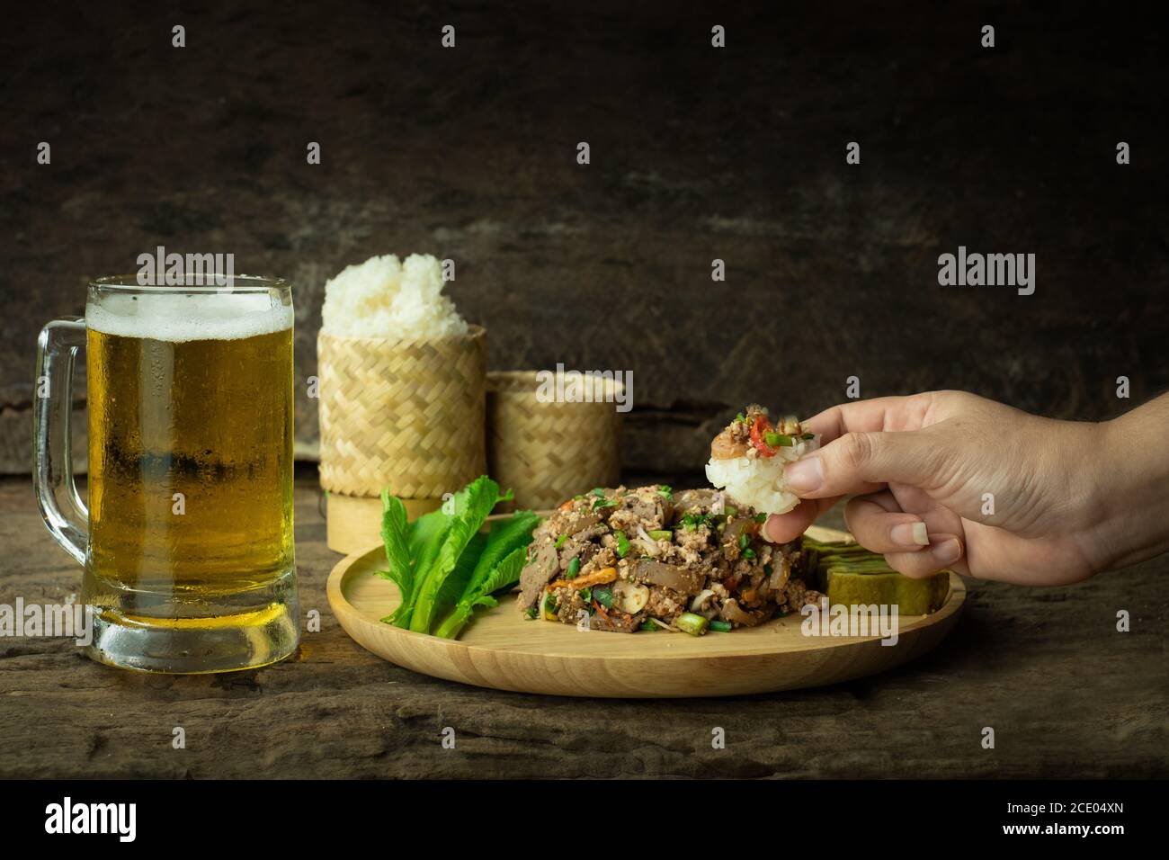 Using a hand to eat sticky rice and spicy minced pork salad with beer