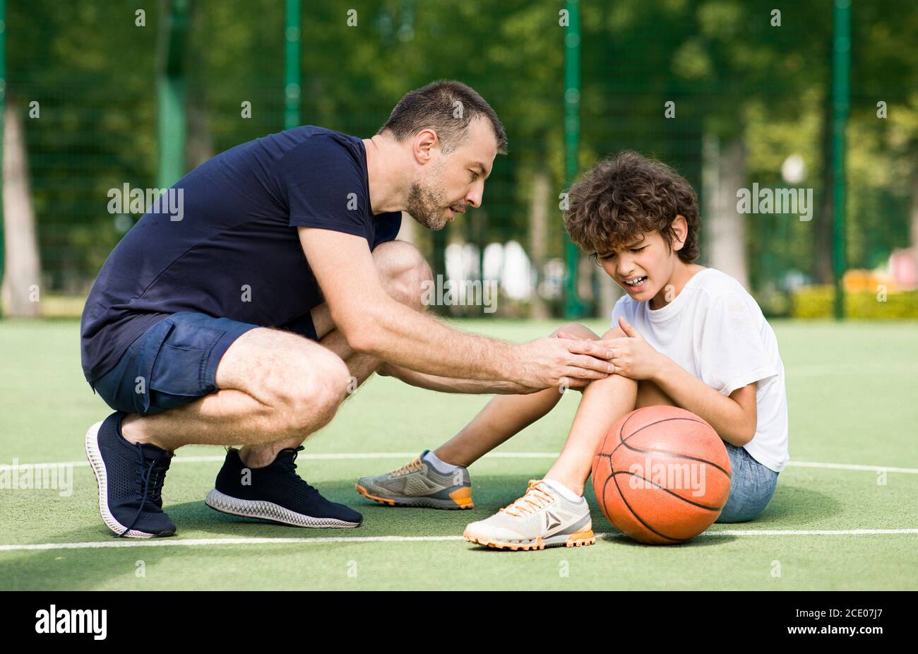 Teacher helping boy with knee trauma after playing basketball Stock
