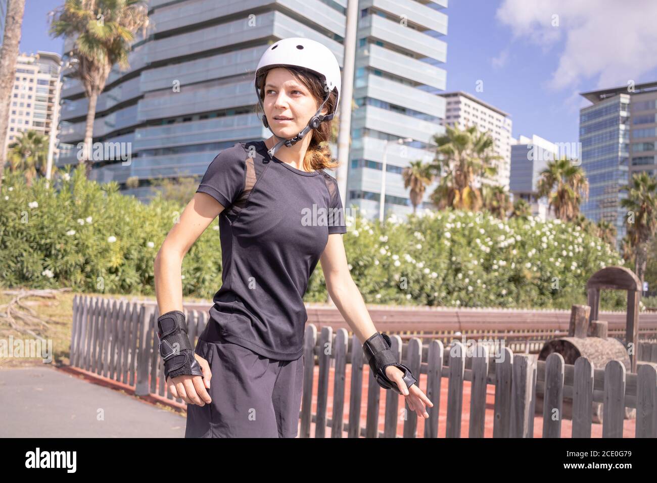 Young roller skater caucasian woman in the white helmet and black sporty clothes, sunny day, skatepark, urban environment. Stock Photo
