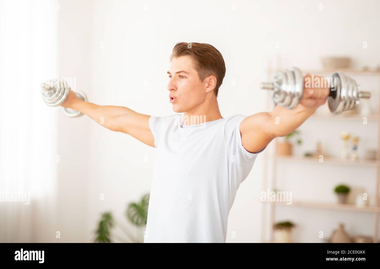 Self-isolation and keep fit. Muscular man lifting dumbbells in daylight Stock Photo