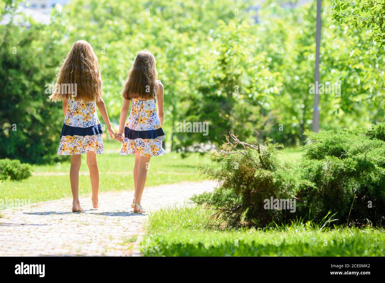 Girlfriends in identical clothes go by the handle in a city park Stock Photo