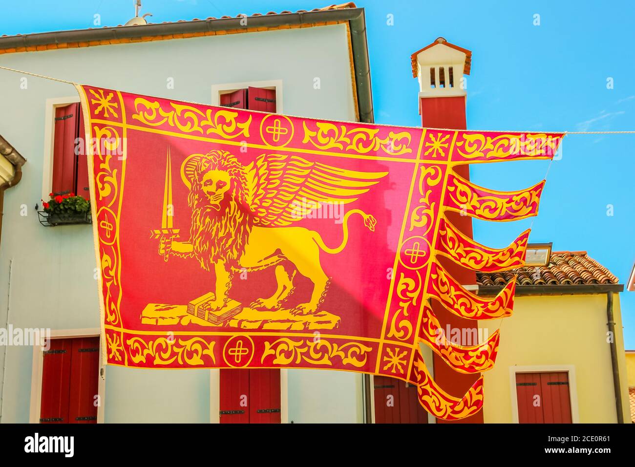 Close-up of San Marco flag, saint Marco, in Italy waving on urban background with Italian style architecture. Red flag of Venice city and Veneto Stock Photo