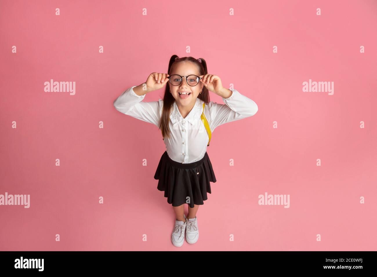 Success in school. Smiling little schoolgirl with glasses and backpack shows tongue and have fun Stock Photo