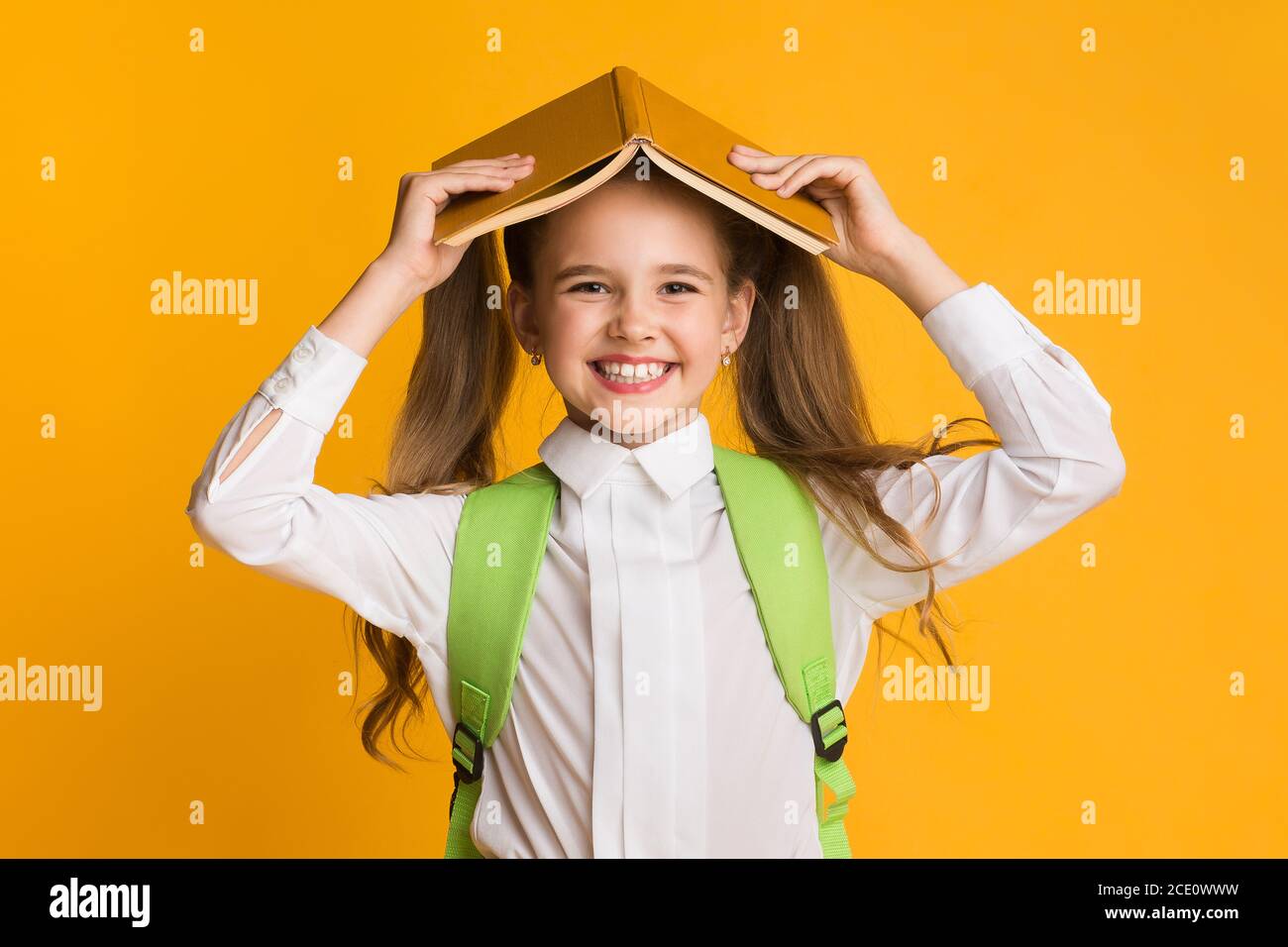 Schoolgirl Holding Book On Head Smiling To Camera, Studio Shot Stock ...