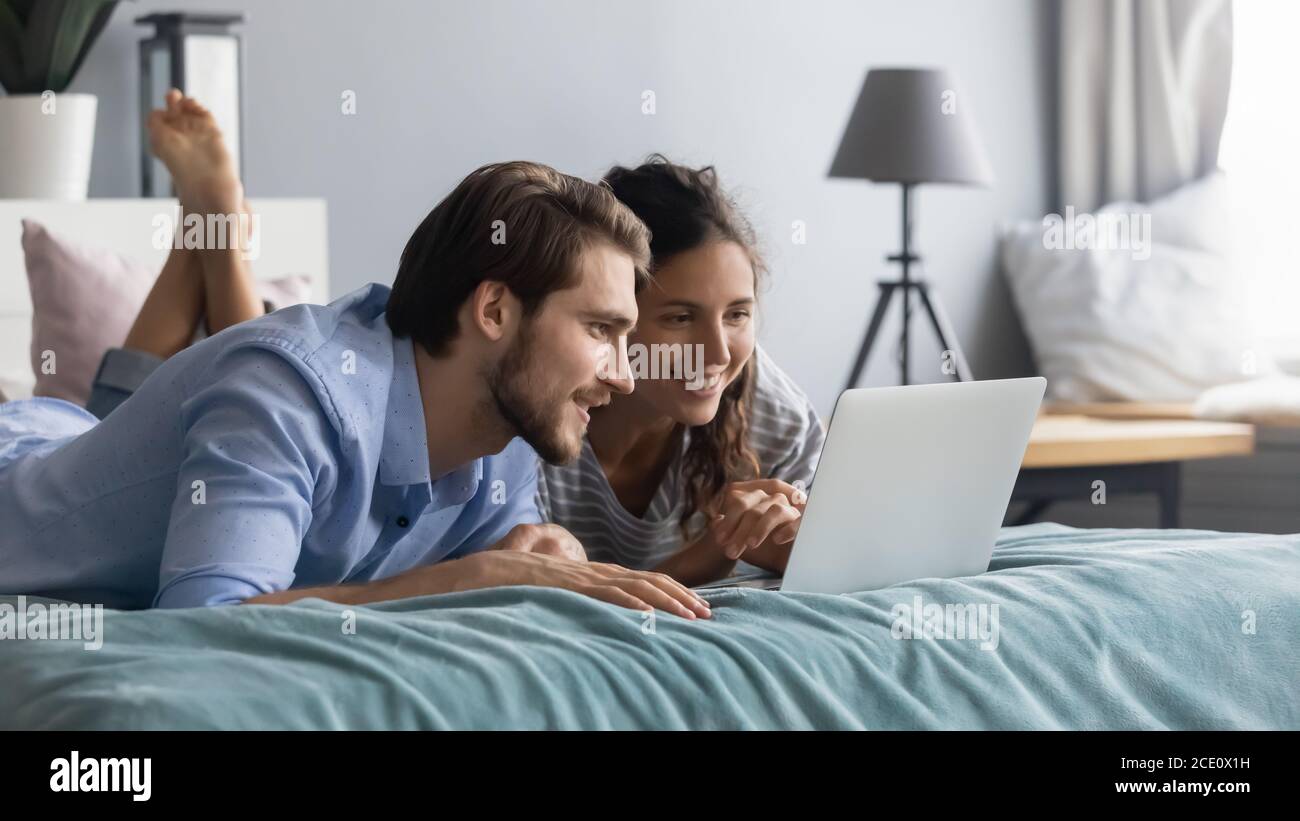 Interested young couple lying on bed, looking at computer screen. Stock Photo