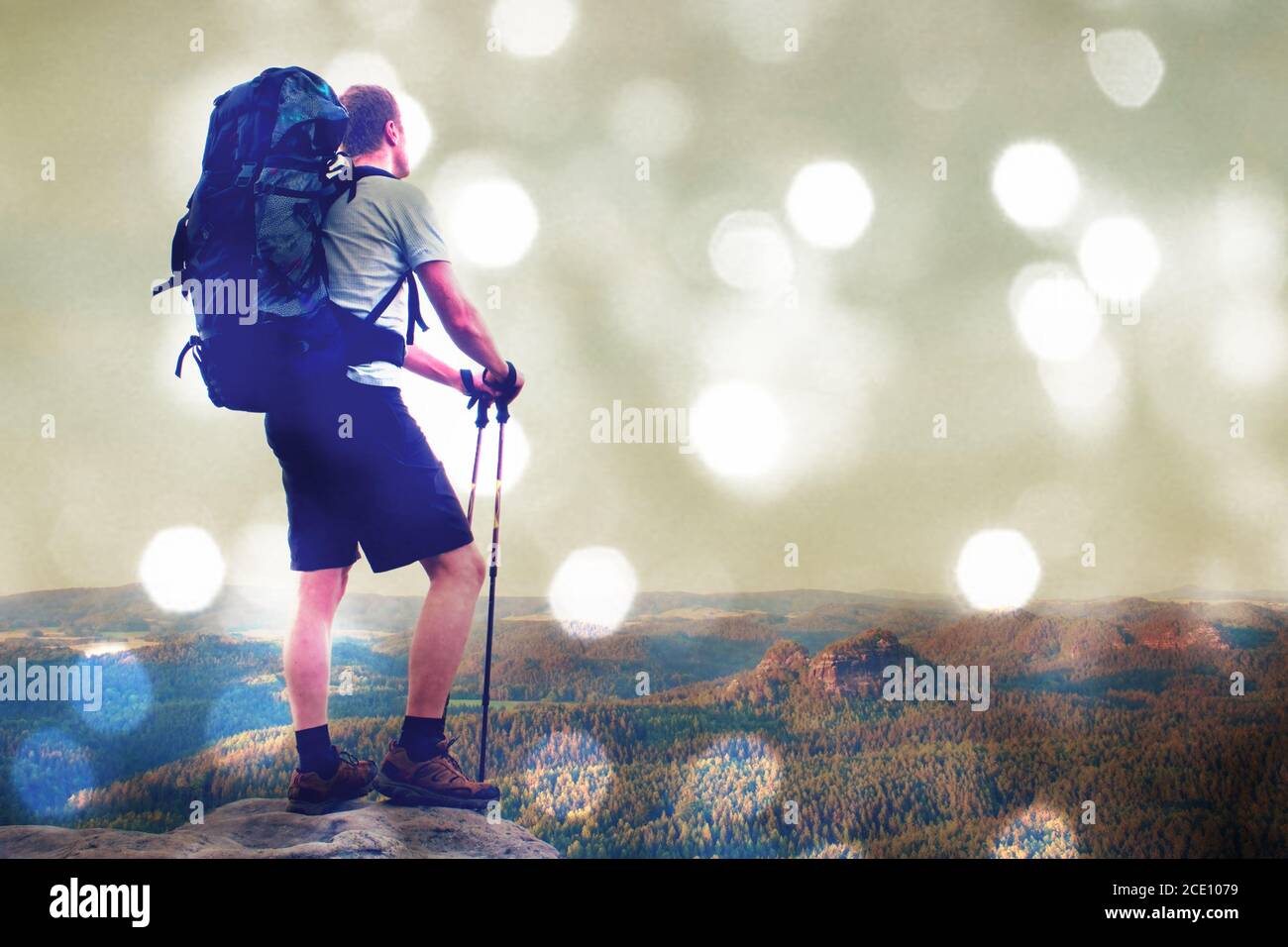 Film effect. Hiker with big backpack stand on rocky view point above misty valley. Stock Photo