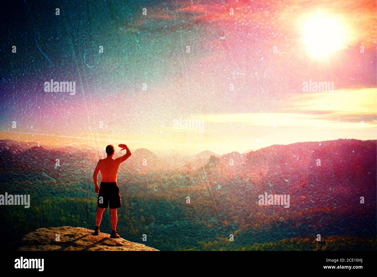 Film grain. Naked man in black pants only at the top of the mountain at Sunset. Dreamy misty valley bellow Stock Photo
