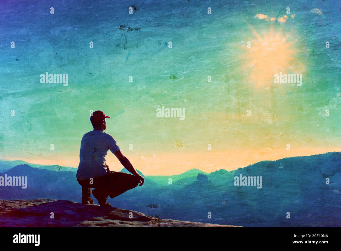 Film grain. Runner in red cap and  in dark sportswear in squatting position on a rock in heather bushes, enjoy the scenery Stock Photo