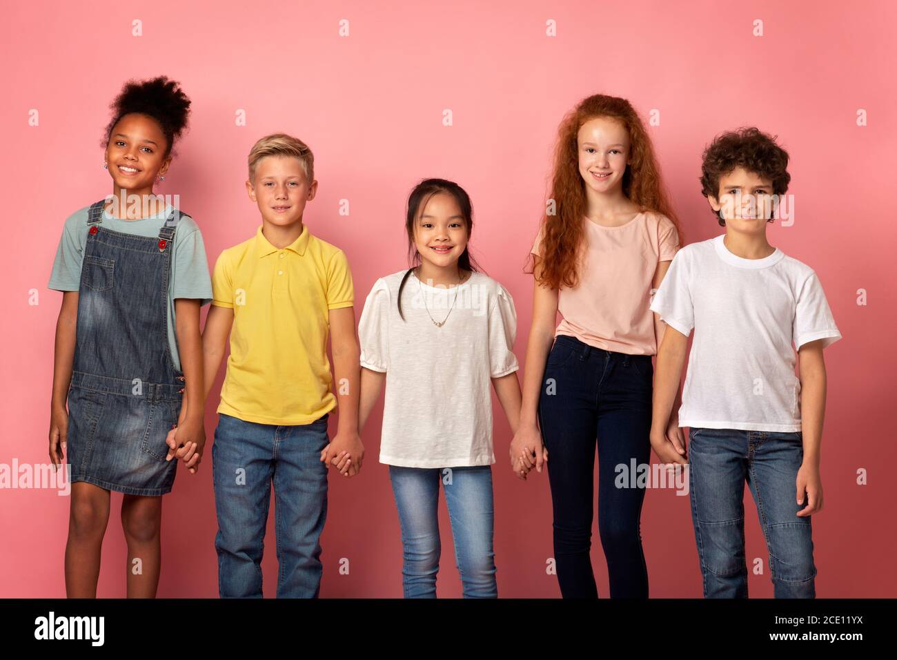 Happy multinational schoolkids holding hands together over pink background Stock Photo