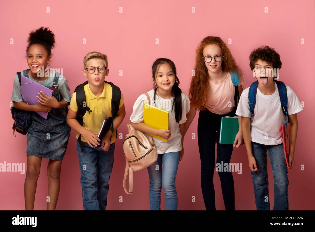 Silly multiethnic kids with school supplies making funny faces on pink background Stock Photo