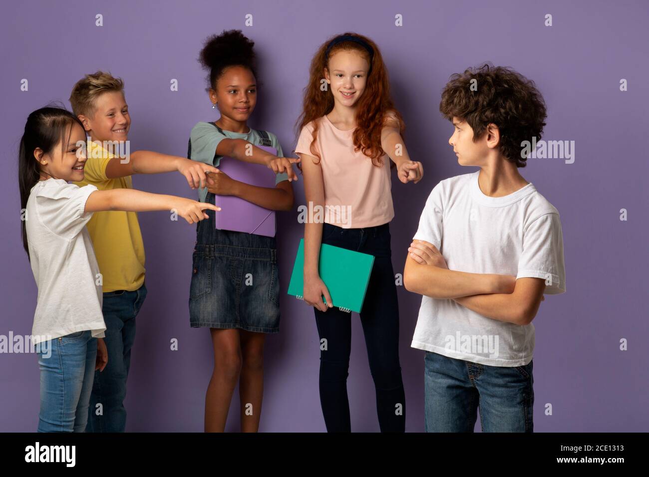 Vicious schoolkids bullying their upset classmate on violet background Stock Photo
