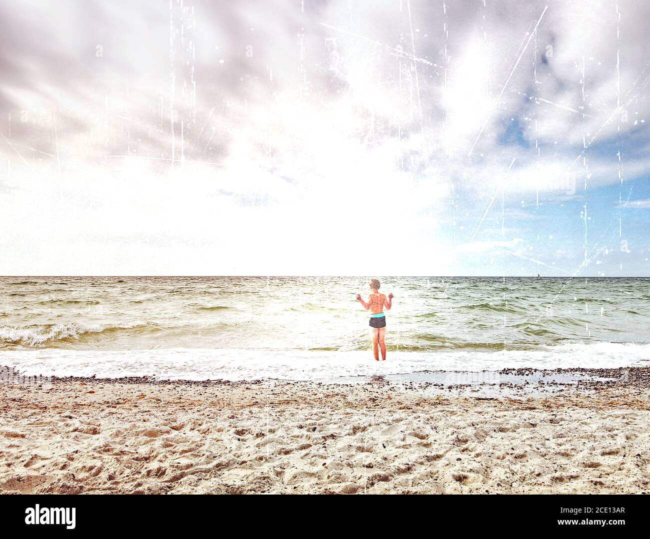 Abstract effect. Blond hair boy stay in cold sea tide. Kid on stony beach with foam Stock Photo