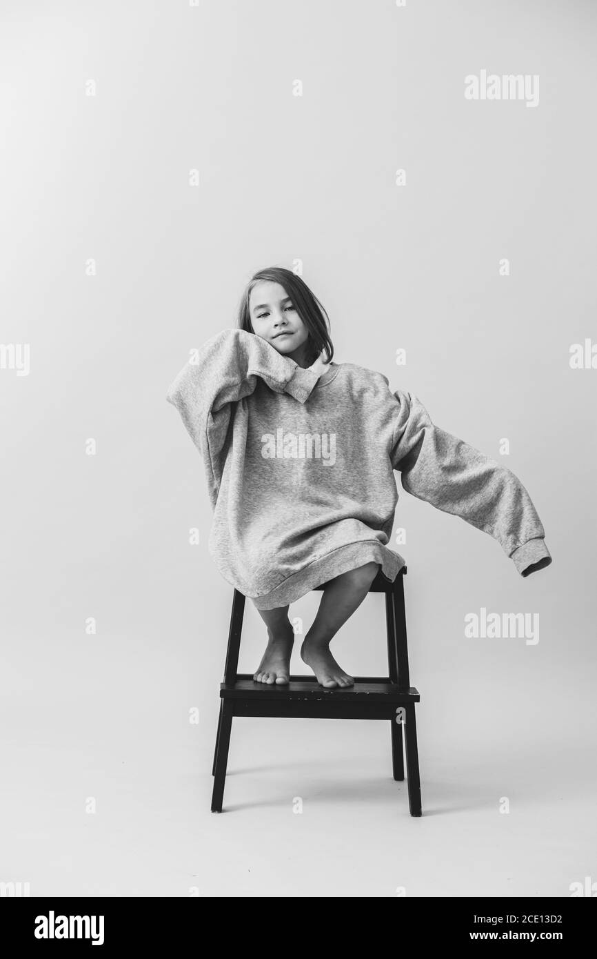 Little girl sitting on the stepping stool in a huge oversized longsleeve Stock Photo